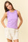 woman wearing a lavender sleeveless top with ruffled neckline and light beige shorts, standing with hands in pockets