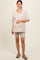 woman wearing a light beige oversized v-neck maternity top and matching bike shorts, holding her baby bump
