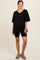 woman wearing a black oversized v-neck maternity top with black bike shorts and styled with casual footwear
