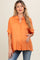 woman wearing an orange short sleeve maternity button-up top and gently holding her baby bump
