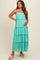 woman wearing a mint green tiered maxi maternity dress with adjustable spaghetti straps and a floral detail, showing baby bump