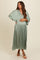 woman wearing a sage green pleated maternity dress with a deep v-neck and flowing sleeves, holding her baby bump