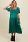 woman wearing a green satin maternity dress with puff sleeves and a ruched bodice, showcasing her baby bump