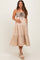 woman wearing a beige maternity dress with a smocked bodice and tiered skirt, holding her baby bump