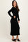 woman wearing a black ribbed long sleeve dress with ruffle hem and pearl button details, smiling and standing in profile