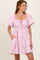 woman wearing a light pink puff sleeve dress with a square neckline and drawstring details, smiling and standing with one hand in the pocket