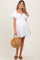 woman wearing a white maternity dress with puff sleeves and a tie detail, holding a straw handbag and showing her baby bump