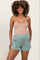 woman wearing a beige maternity tank top and light green maternity shorts with pockets, showing a baby bump