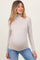 woman wearing a light beige long sleeve maternity turtleneck top and showing her baby bump