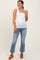woman wearing a white ribbed tank top and light blue flared jeans, showcasing her baby bump