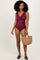 woman wearing a burgundy ruffled one-piece swimsuit, holding a straw bag, with curly hair and sandals