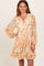 woman wearing a floral print orange and white long sleeve dress with a v-neck and tiered skirt