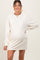 woman wearing a cream long sleeve maternity dress with a visible baby bump and smiling at the camera