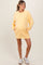 woman wearing a yellow maternity oversized sweatshirt dress with pockets and a visible baby bump