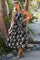 woman wearing a black and white floral print sleeveless maxi dress, standing outdoors among tropical plants