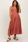 woman wearing a rust colored maternity dress with ruffle straps and a tiered skirt, standing and smiling