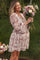 woman wearing a floral blush maternity dress and holding a bouquet of flowers with a visible baby bump