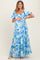 woman wearing a blue and white floral maternity maxi dress and holding her baby bump