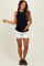woman wearing a black sleeveless maternity top and white shorts, showing her baby bump while smiling