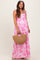 woman wearing a pink floral maternity maxi dress with spaghetti straps and holding a woven bag, showing her baby bump
