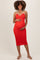 woman wearing a red ribbed maternity dress with halter straps and holding her baby bump