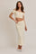 woman wearing a cream off-the-shoulder crop top and a matching long skirt, styled with white shoes