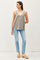 woman wearing a light gray spaghetti strap tank top with a v-neck and blue skinny jeans, standing against a plain background