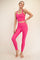 woman wearing a bright pink sports bra and matching high-waisted leggings, smiling and standing barefoot