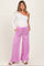 woman wearing a white one-shoulder maternity top and pink wide-leg maternity pants with pockets