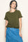 woman wearing a dark green short sleeve top with ruffle details and a denim skirt, smiling at the camera