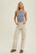 woman wearing a light blue ribbed tank top and cream high-waisted jeans, standing with hands in pockets