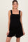 woman wearing a black smocked maternity romper with wide straps and a relaxed fit, showing her baby bump