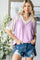 woman wearing a lavender short sleeve top with crochet detail and distressed denim shorts, standing in a bright room