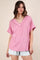 woman wearing a pink short sleeve v-neck top with a textured pattern and casual style, paired with light denim shorts