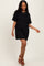 woman wearing a black oversized t-shirt dress and brown heeled sandals, posing with one hand on her hip