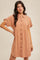 woman wearing a rust-colored short sleeve button-up dress with a cinched waist and relaxed fit