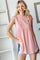 woman wearing a light pink sleeveless top with a textured fabric and a relaxed fit, paired with denim shorts