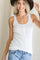 woman wearing a white ribbed tank top with button details and a wide-brimmed hat, smiling while posing