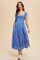 woman wearing a blue floral midi dress with a smocked bodice and cap sleeves, standing and smiling