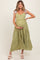 woman wearing a light green maternity dress with floral embroidery and ruffled tiers, holding her baby bump