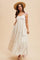 woman wearing a creamy white floral maxi dress with a smocked bodice and shoulder ties, accessorized with a straw hat