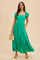 woman wearing a vibrant green maxi dress with puff sleeves and pockets, holding a straw bag