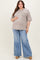woman wearing a light brown oversized maternity top with a pocket and flared blue jeans, showing her baby bump
