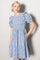 woman wearing a blue floral print short dress with puff sleeves and a tiered skirt, posing with one hand in a pocket