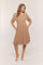 woman wearing a taupe puff sleeve dress with pockets and a fitted bodice, standing with one hand in pocket