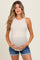 woman wearing a light beige maternity tank top and holding her baby bump, paired with denim shorts