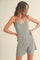 woman wearing a light gray ribbed tank romper with a v-neck and fitted silhouette