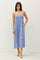 woman wearing a blue patterned sundress with thin straps and pockets, standing against a plain background
