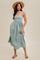 woman wearing a light blue sleeveless midi dress with a gathered waist and a natural straw hat