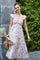 woman wearing a floral print maxi dress with ruffle sleeves, smiling and holding a bouquet of flowers